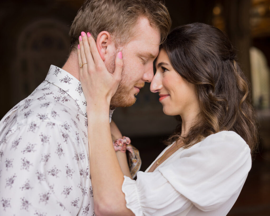 Bride-to-be holding her fiancé’s face as they share a quiet, intimate moment under Bethesda Terrace during their rainy spring engagement session in Central Park.