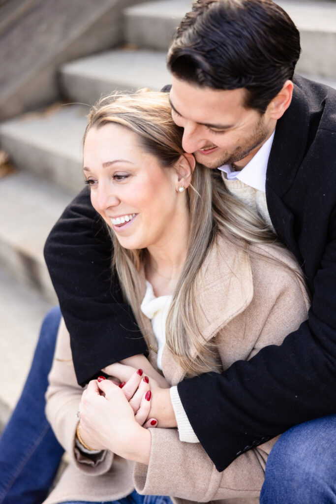 Close-up of engaged couple seated on Central Park steps, sharing a warm embrace during their winter session.