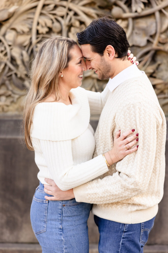 Engaged couple in cream sweaters sharing an intimate forehead-to-forehead moment during their Central Park winter engagement session.