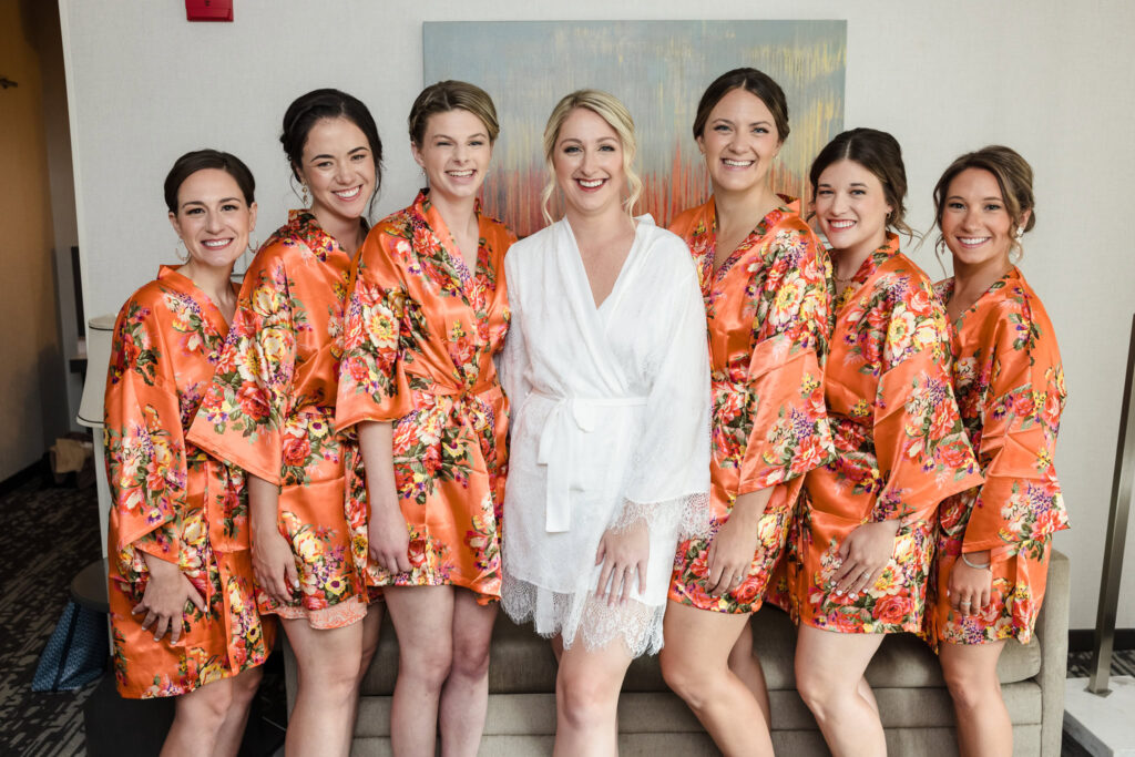 Bride surrounded by bridesmaids in vibrant floral robes during a joyful wedding morning at her Crescent Beach Club September wedding on Long Island, capturing connection before the waterfront celebration.