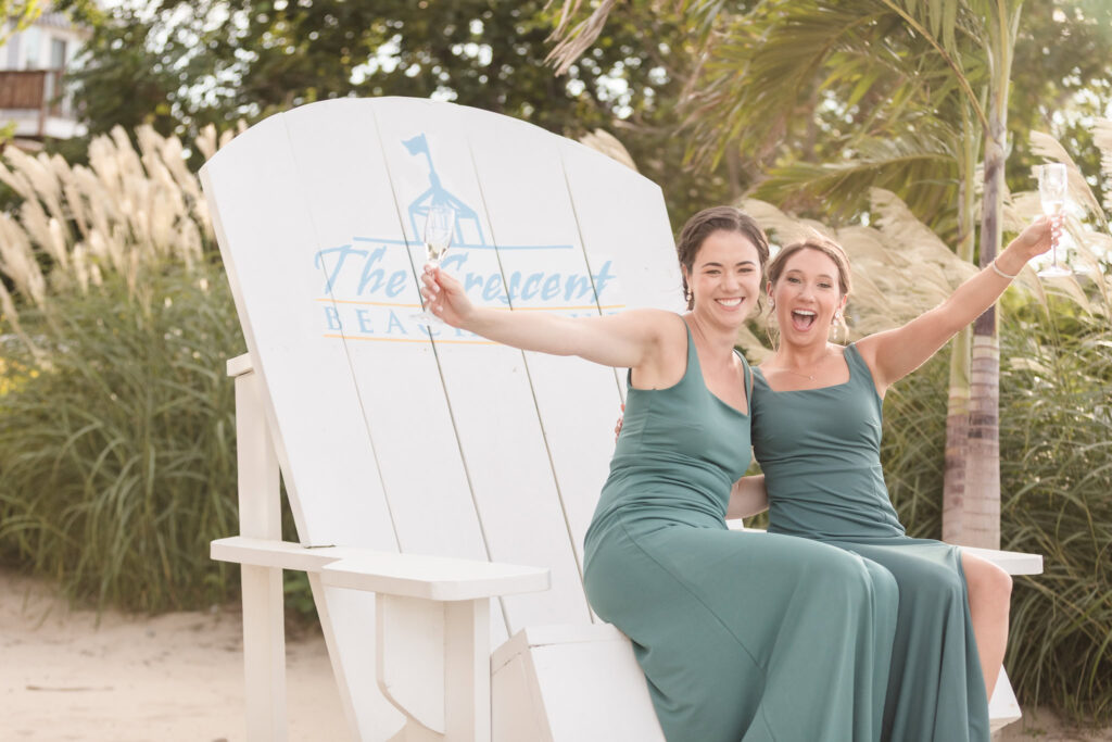Bridesmaids celebrating with champagne on Crescent Beach Club’s signature oversized chair, adding playful energy to this joyful wedding on Long Island’s waterfront.