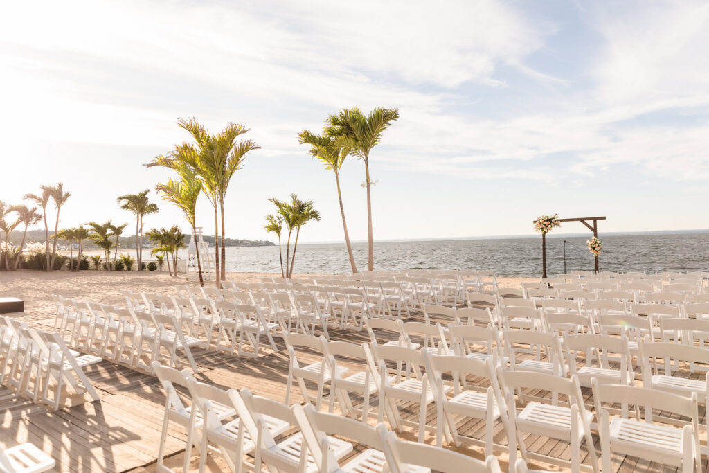 Elegant beachfront ceremony setup at Crescent Beach Club with white chairs and floral arch overlooking the Long Island Sound, ready for a serene September wedding celebration.