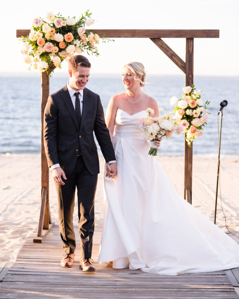 Bride and groom walk hand-in-hand down the aisle, beaming after their Crescent Beach Club beach wedding ceremony, surrounded by golden September light and Long Island’s waterfront views.