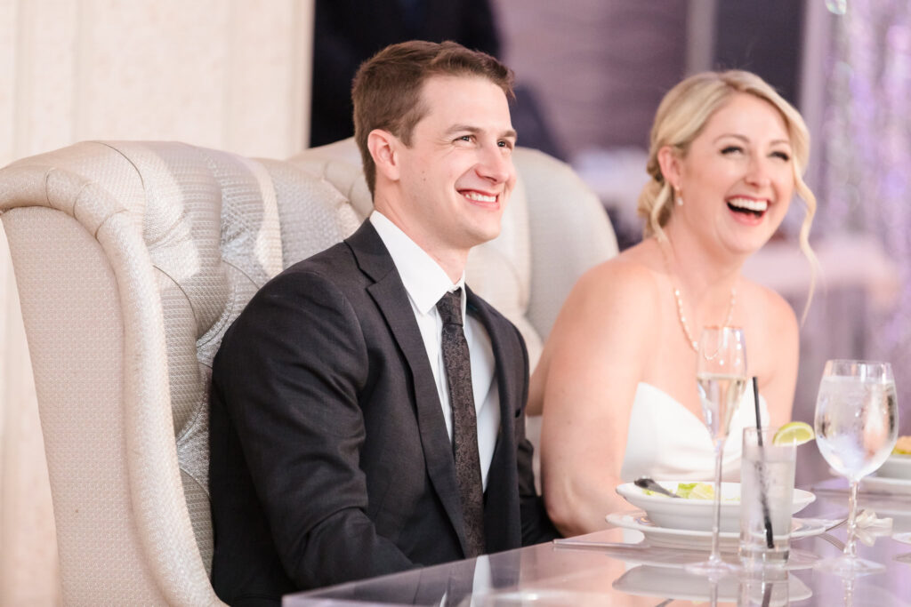 Bride and groom laugh together at their sweetheart table during the reception at Crescent Beach Club, enjoying heartfelt moments during their elegant September wedding on Long Island.