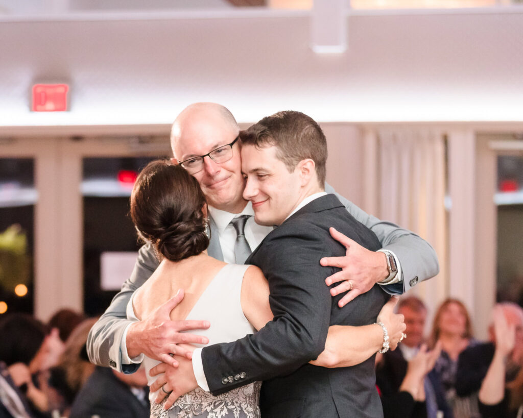 Groom embraces his parents during an emotional moment at the reception, capturing the warmth and connection of a September wedding on Long Island.