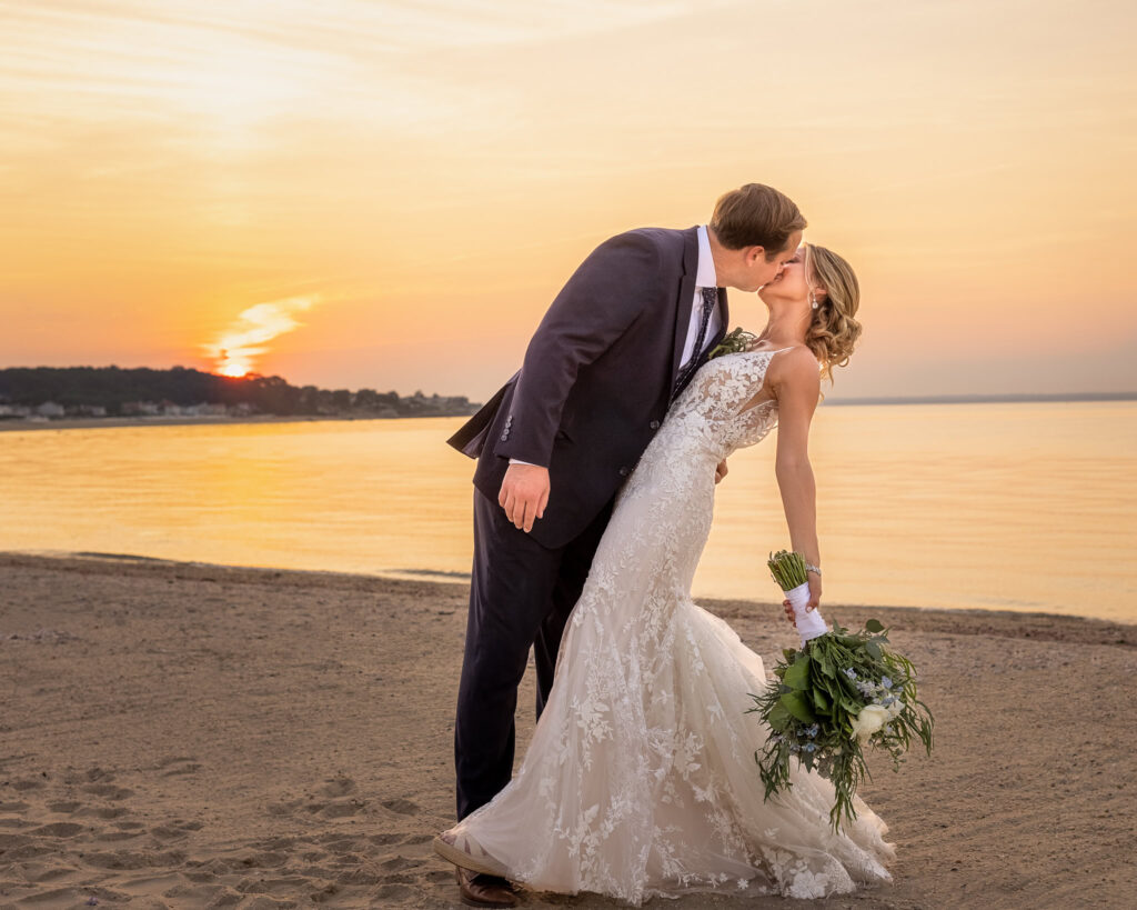 Bride and groom share a kiss during sunset portraits on the beach at a Crescent Beach Club waterfront wedding, with warm golden light reflecting across the water.