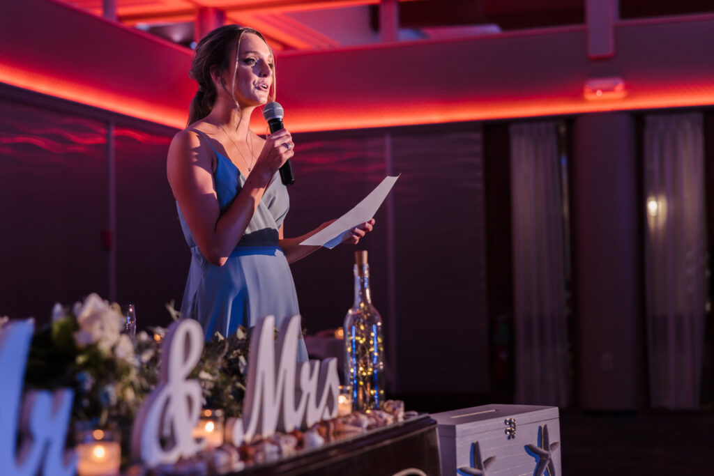 Bridesmaid delivers a heartfelt toast during the reception at a Crescent Beach Club waterfront wedding, standing at the head table with warm uplighting and wedding décor in view.
