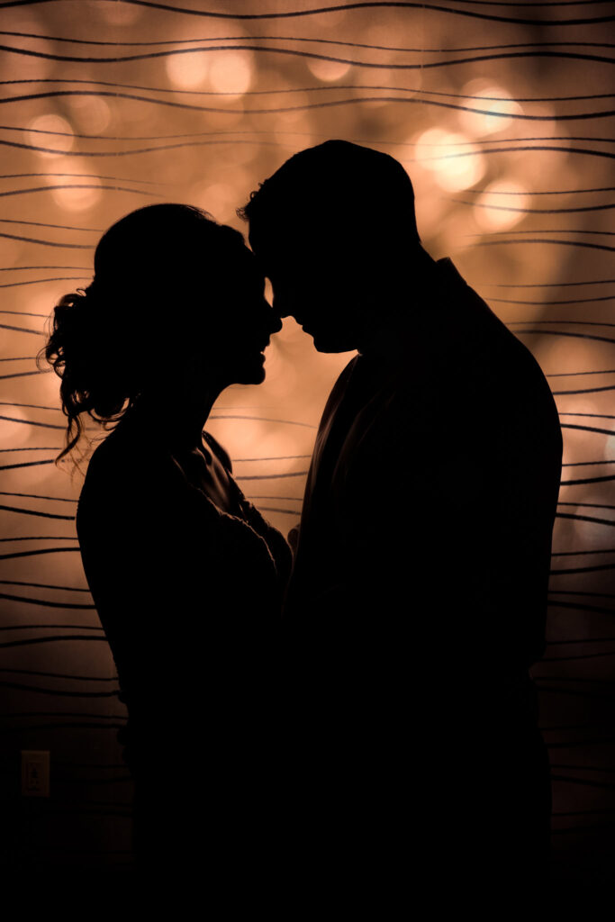 Silhouetted bride and groom share a quiet moment during the reception at a Crescent Beach Club waterfront wedding, framed against softly glowing bokeh lights in the background.