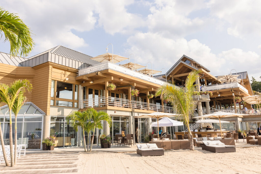 Exterior view of Crescent Beach Club on Long Island, featuring beachfront lounge areas, palm trees, and a modern coastal design with open terraces and umbrellas.