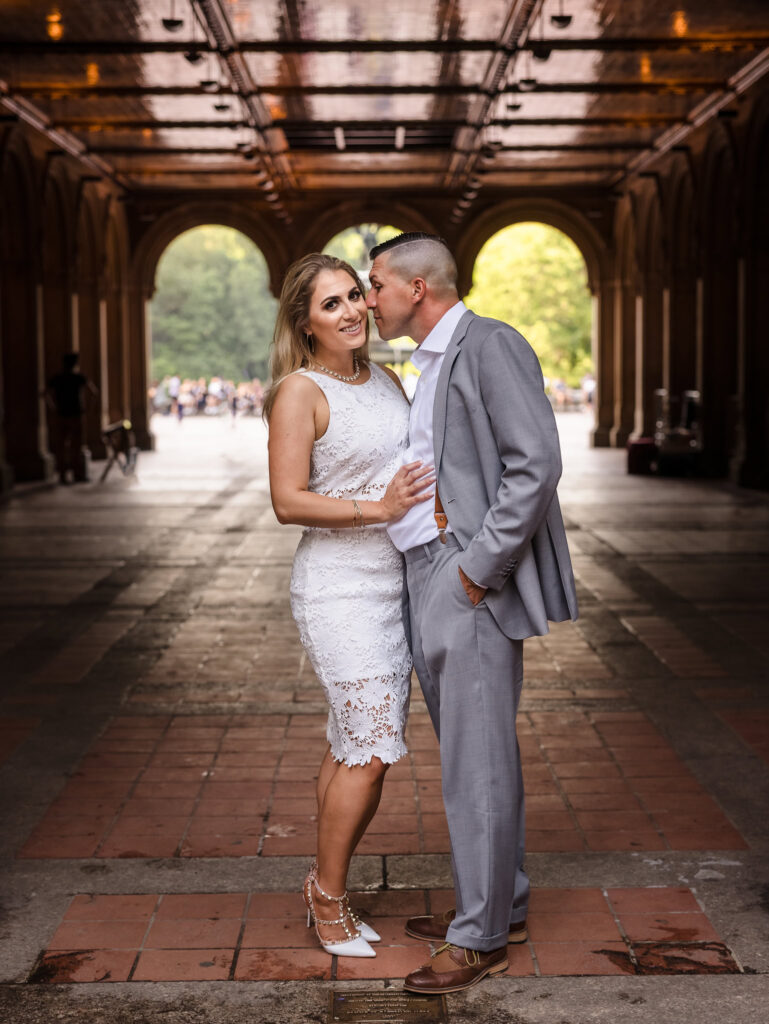 Couple posing under the arches at Bethesda Terrace during their editorial engagement session in Central Park, styled in a white lace dress and grey suit for a refined, fashion-inspired look.