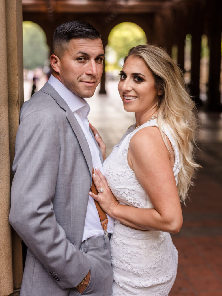 Close-up of couple leaning against stone column at Bethesda Terrace, showcasing polished fashion and engagement ring during their editorial engagement session in Central Park.
