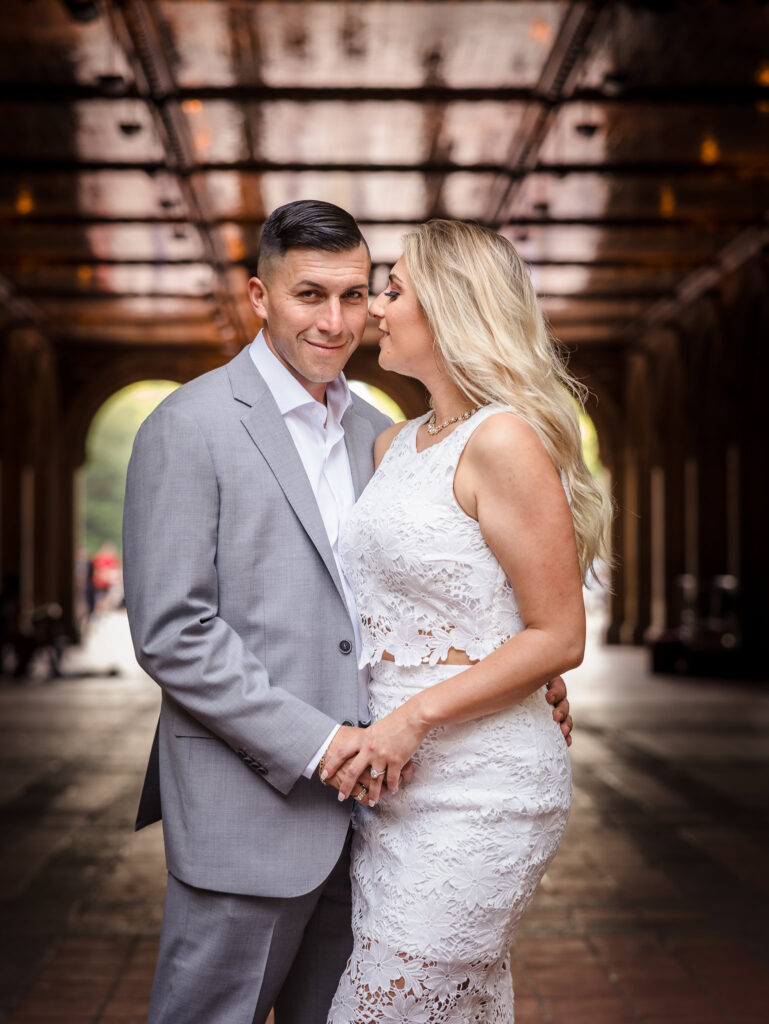 Bride-to-be whispers to her fiancé under the reflective ceiling of Bethesda Terrace, blending romantic energy with an editorial style engagement photo in Central Park.