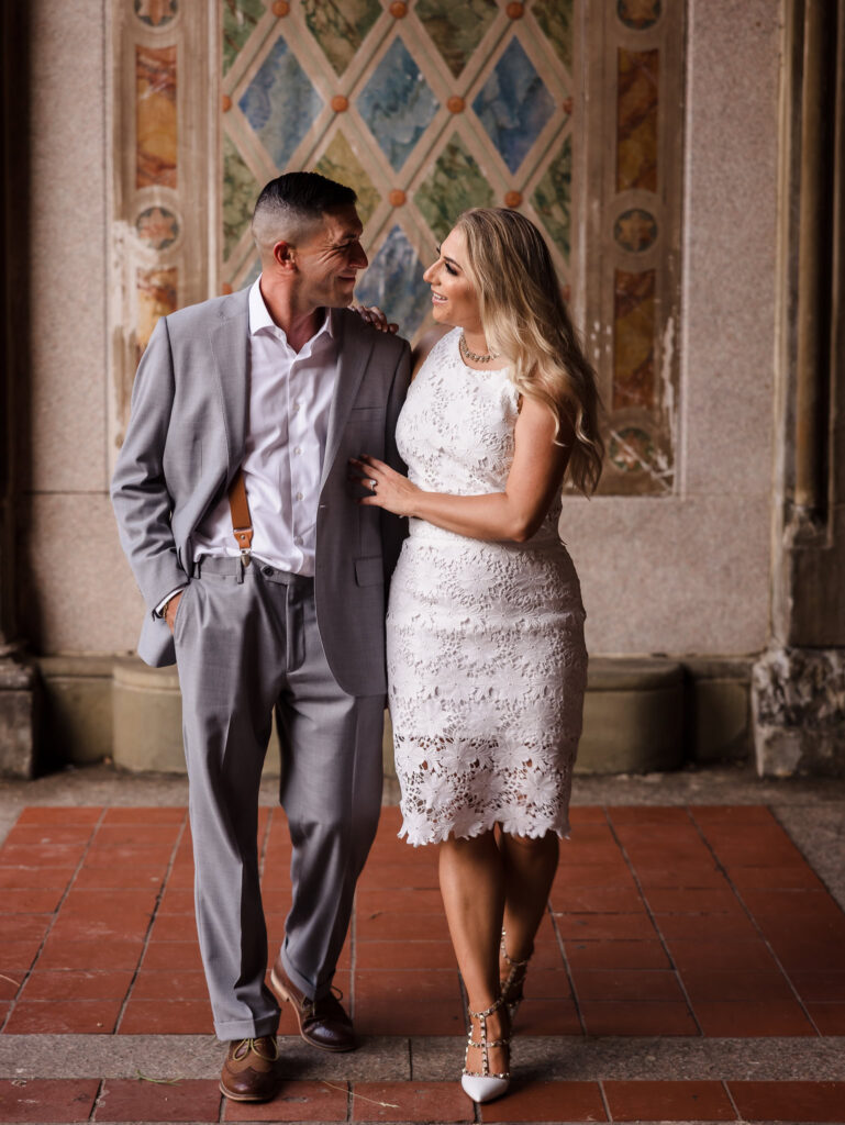 Engaged couple walks arm in arm beneath the Minton tile murals at Bethesda Terrace, showcasing refined style during their editorial engagement session in Central Park.