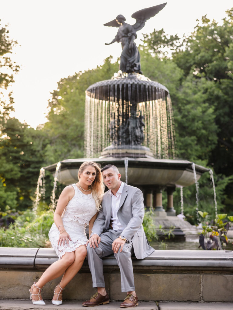 Engaged couple seated in front of Bethesda Fountain during their editorial engagement session in Central Park, dressed in refined neutral attire with a fashion-forward aesthetic.