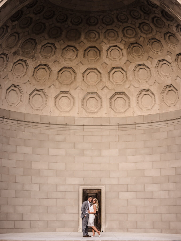 Editorial engagement session in Central Park with couple posed beneath the architectural dome of Naumburg Bandshell, showcasing refined style and composition.