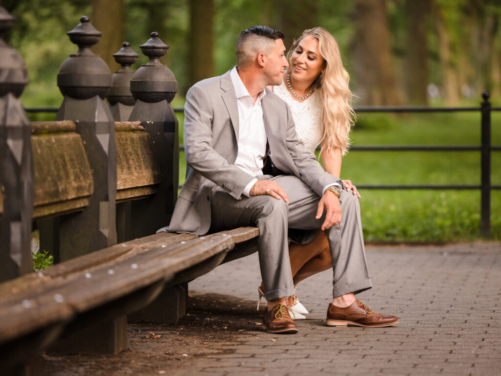 Couple seated on a rustic bench along The Mall in Central Park, sharing a quiet, affectionate moment during their luxury editorial engagement session.