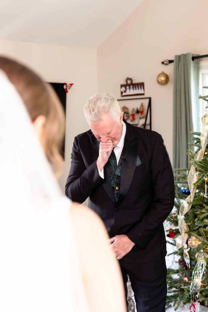 Father of the bride overcome with emotion during a heartfelt first look with his daughter on her wedding day beside a decorated Christmas tree.