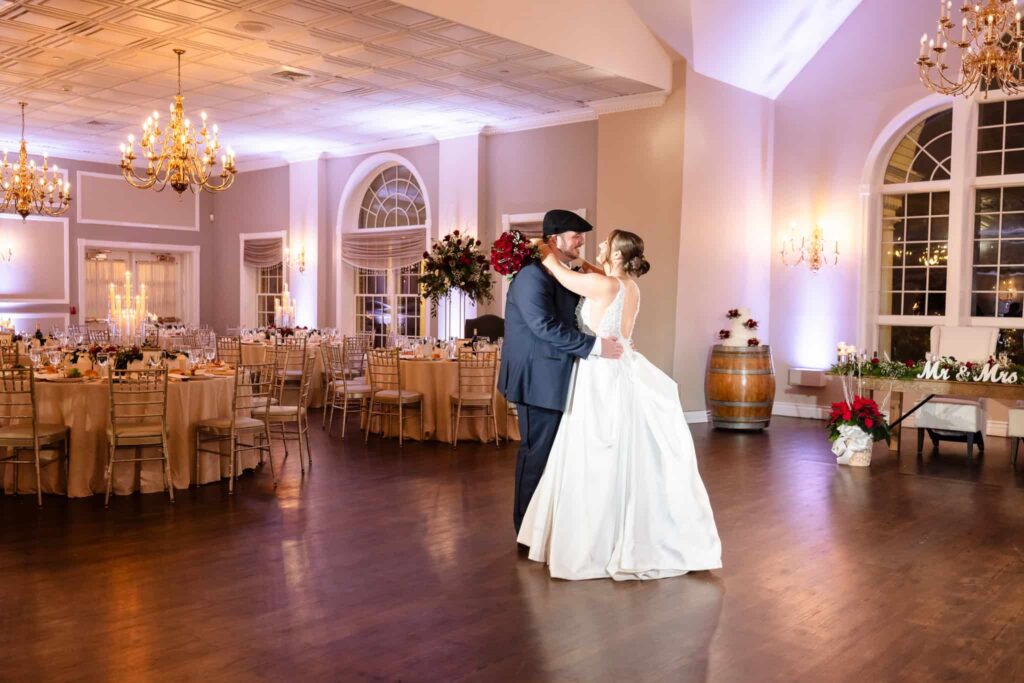 Bride and groom sharing their first dance in an elegant ballroom with soft candlelight, holiday florals, and romantic gold decor during their winter wedding reception.