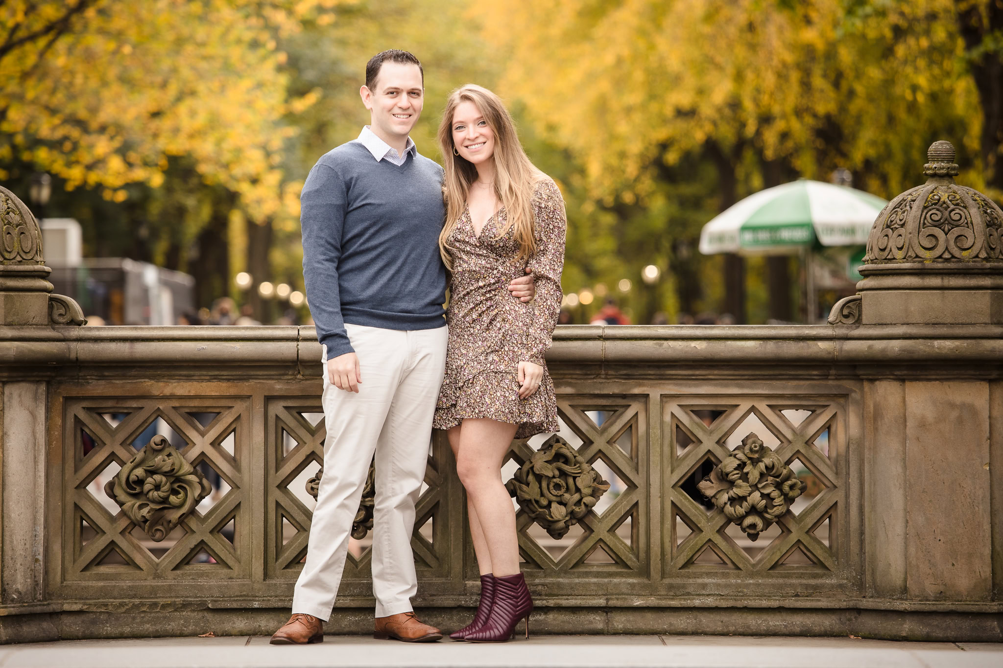 Engaged couple standing at Bethesda Terrace in Central Park during their fall engagement session, framed by golden autumn leaves and classic stonework in NYC.
