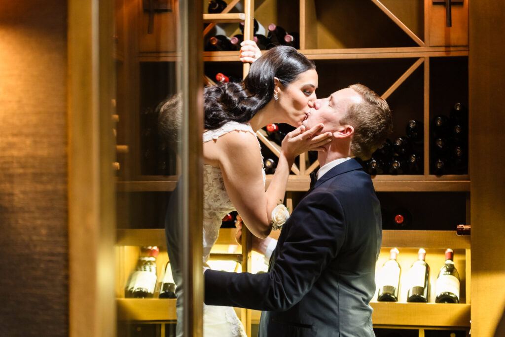 Bride and groom share an intimate kiss in the wine cellar in Islip, NY a romantic and refined moment captured among glowing bottles and warm wood shelving.
