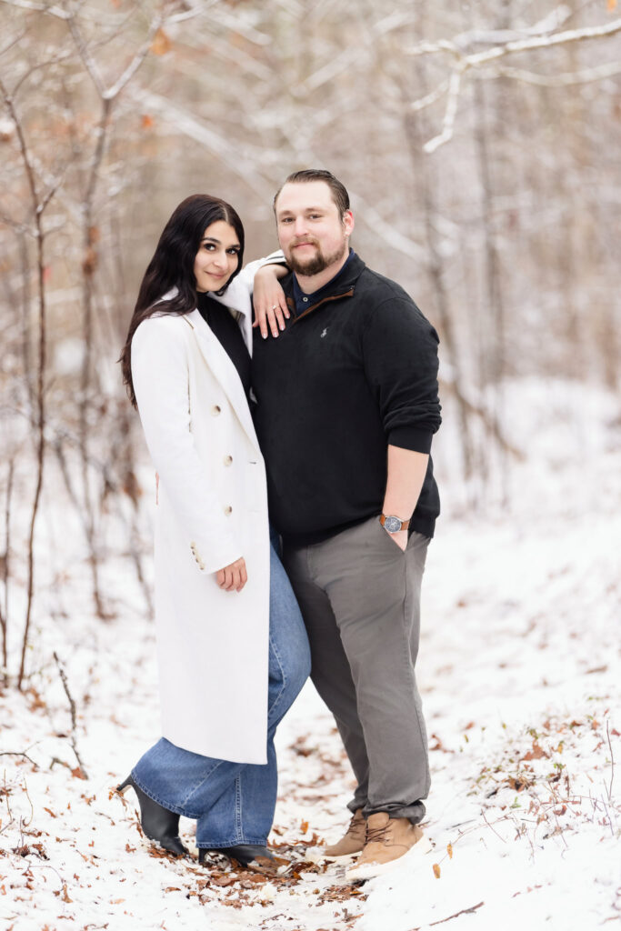 Engaged couple posing confidently in the snow at Bethpage State Park, with the bride-to-be resting her arm on her fiancé’s shoulder and showcasing her engagement ring.