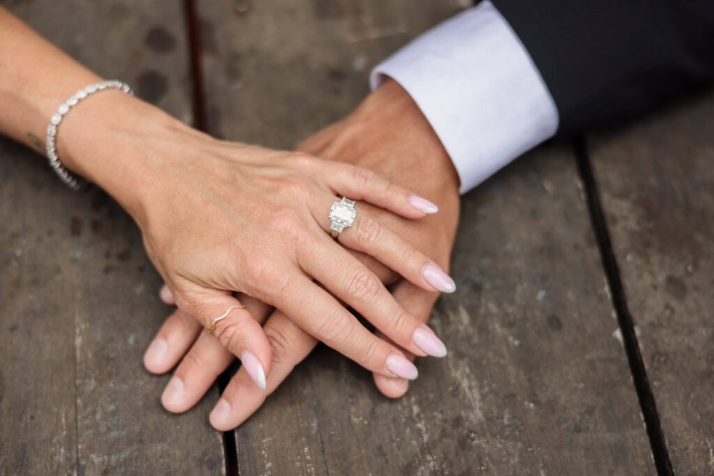 Close-up of engagement ring and intertwined hands during a Brooklyn waterfront engagement session in DUMBO, highlighting refined detail photography during the best time for a DUMBO engagement session.