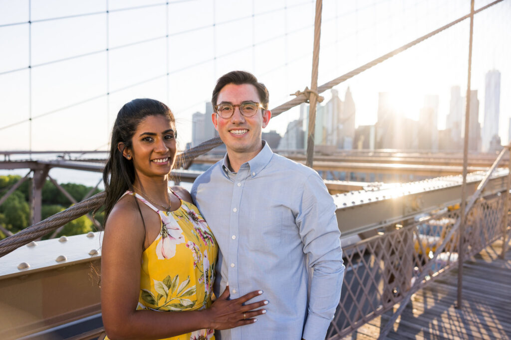 Brooklyn Bridge engagement photos in DUMBO featuring Sreetha and Demitri during golden hour on the bridge, with warm evening light in Brooklyn and a soft Brooklyn skyline backdrop highlighting her yellow dress.