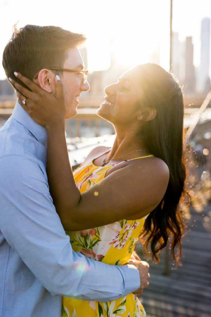 Close-up of couple embracing on the Brooklyn Bridge with glowing backlight, emphasizing golden hour engagement photography in NYC.
