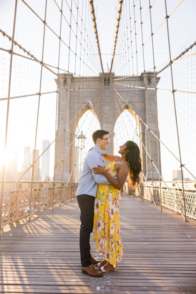 Romantic couple embracing on the Brooklyn Bridge at golden hour, framed by symmetrical suspension cables for timeless NYC architectural engagement photos.