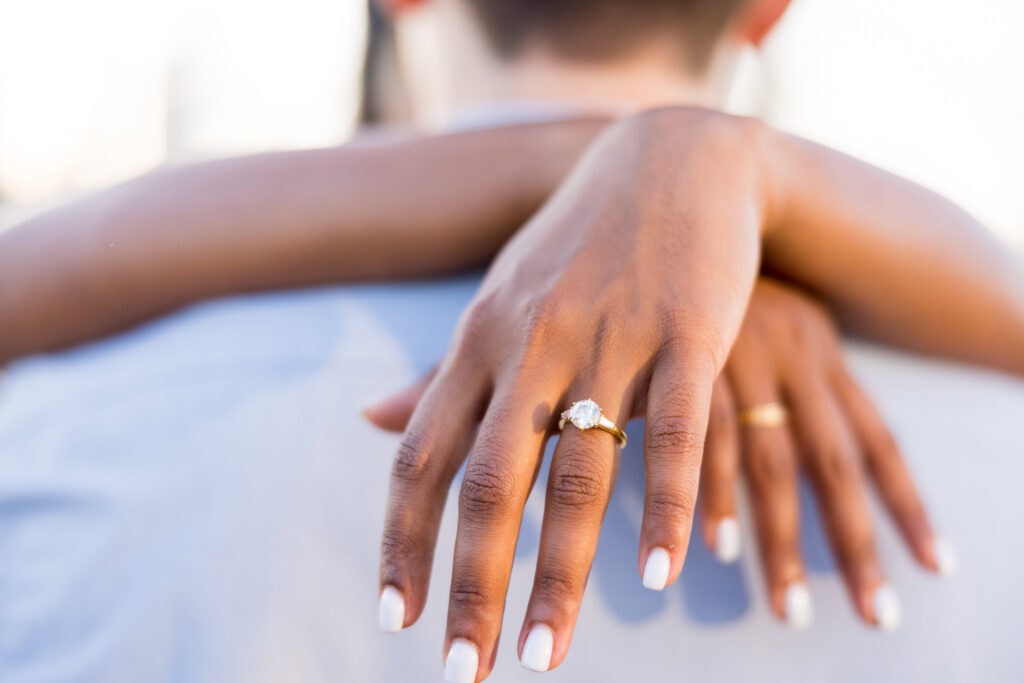 Close-up engagement ring detail, featuring a round diamond on a gold band with soft golden hour light and shallow depth of field.