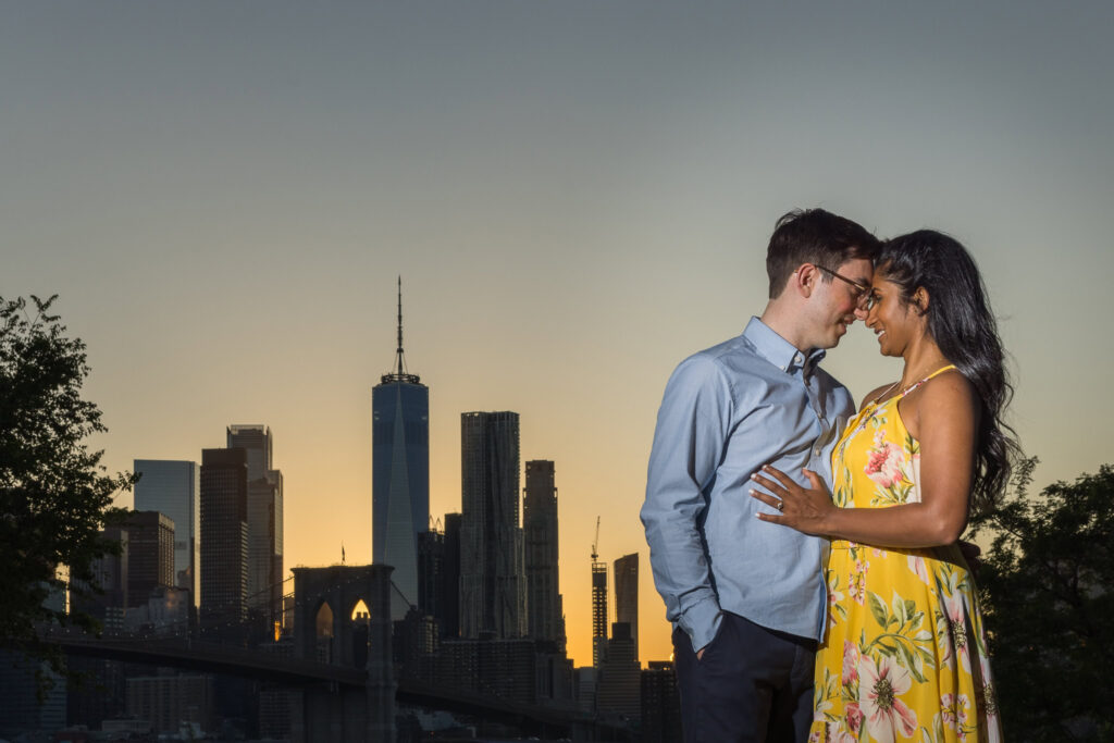 Romantic sunset portrait with One World Trade Center and Brooklyn Bridge in the background, demonstrating the Best time for a DUMBO engagement session at dusk.