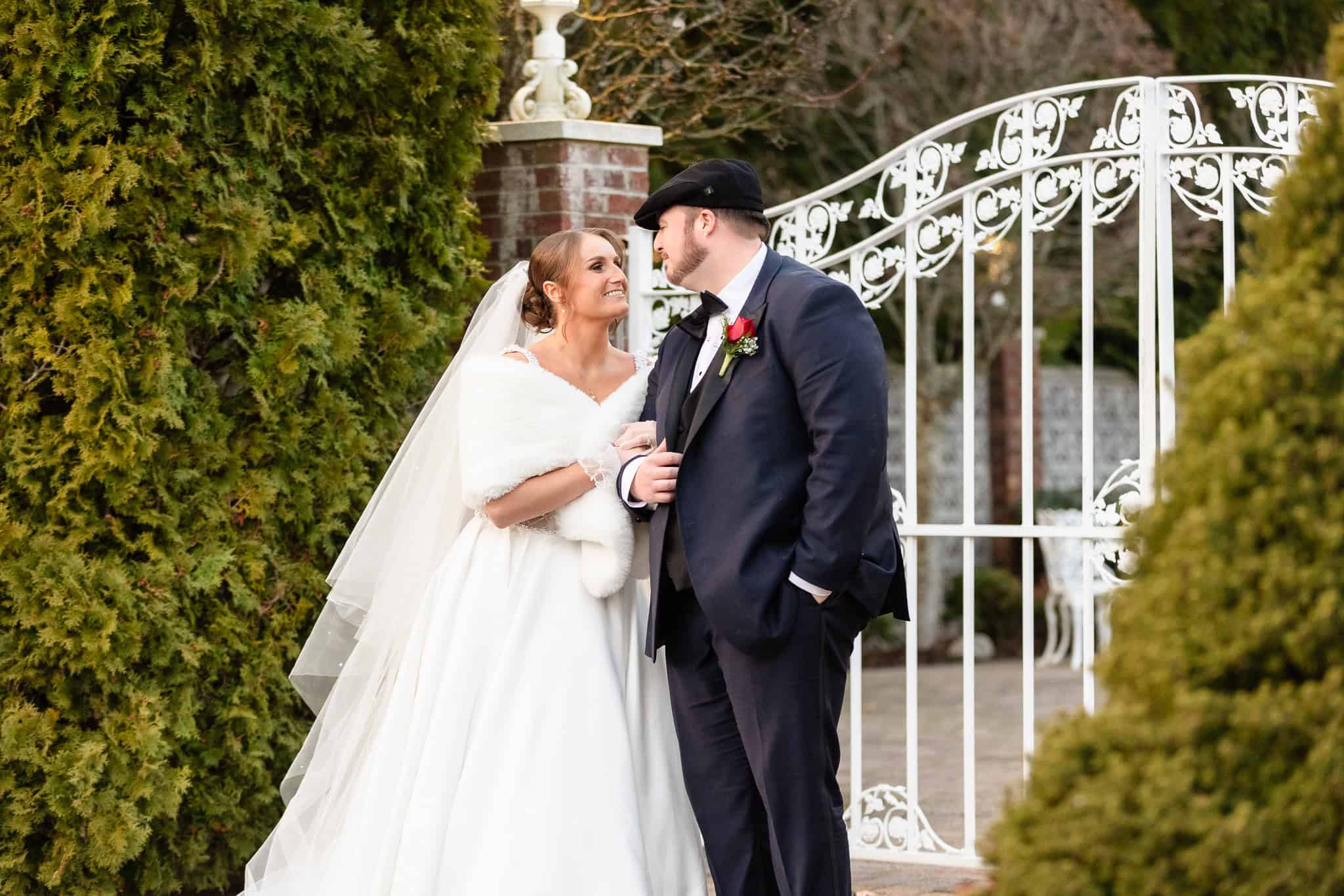 Winter wedding portrait of the bride and groom at the Estate at East Wind, standing together by the garden gate in a timeless Long Island setting.
