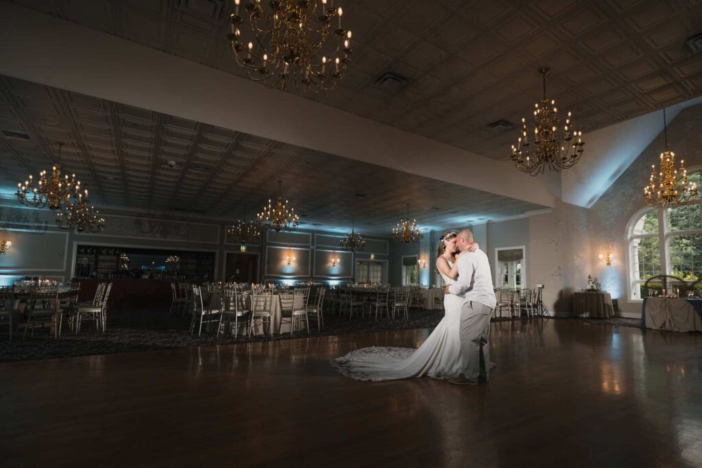Bride and groom sharing a quiet dance inside the Estate at East Wind ballroom, surrounded by chandeliers and formal reception seating during a classic Long Island wedding.