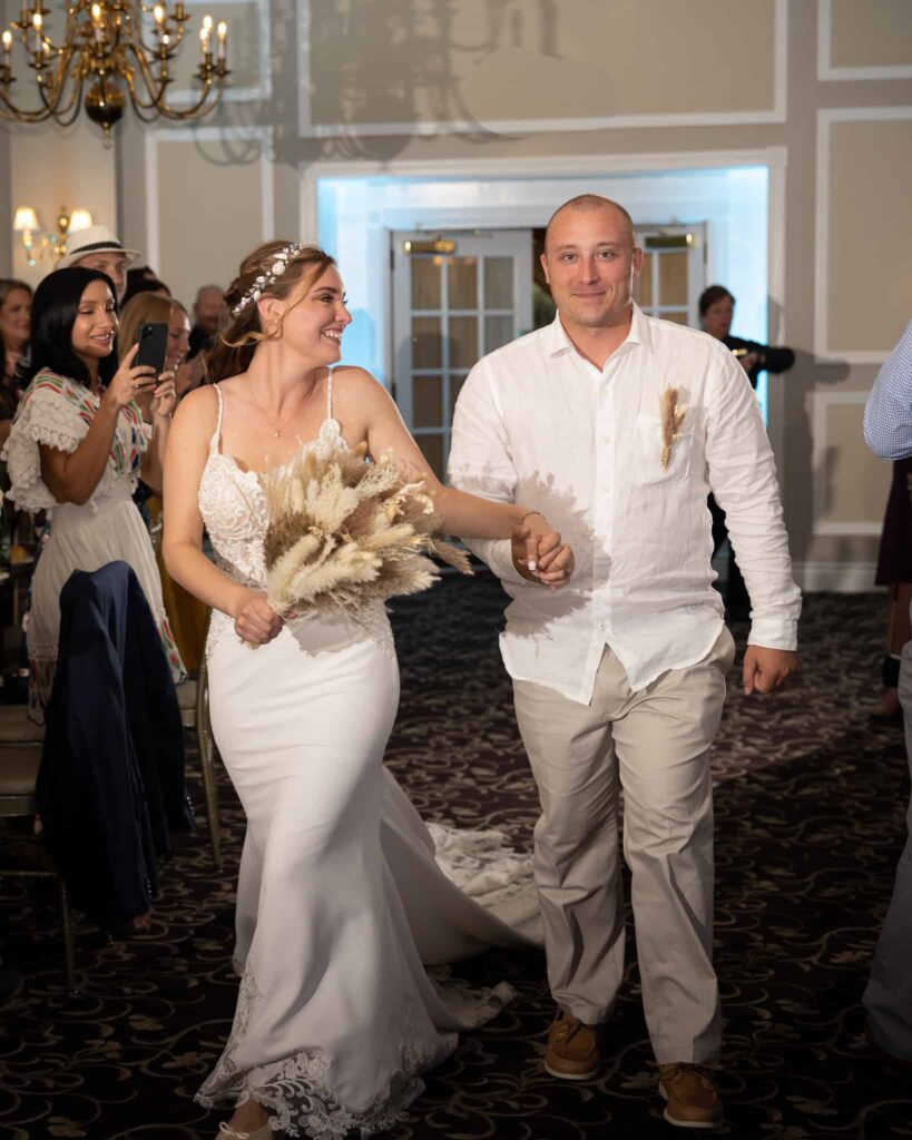 Bride and groom entering their Estate at East Wind wedding reception hand in hand, smiling as guests celebrate inside the elegant Long Island ballroom.