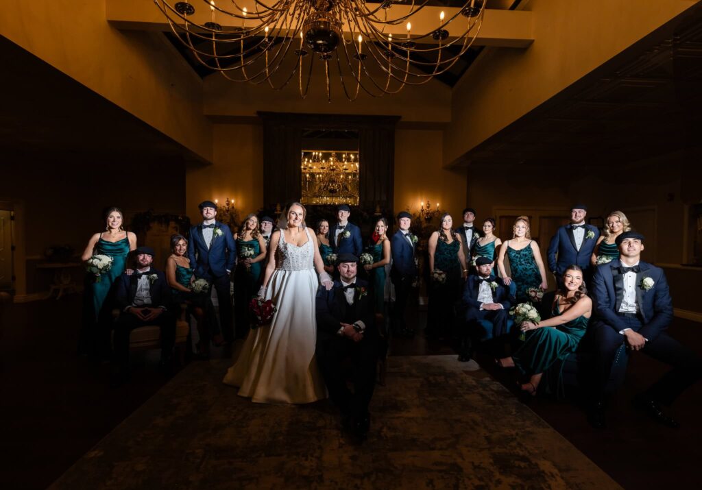 Formal wedding party portrait at an Estate at East Wind wedding, featuring the bride and groom surrounded by their bridal party beneath grand chandeliers during an elegant Long Island reception.