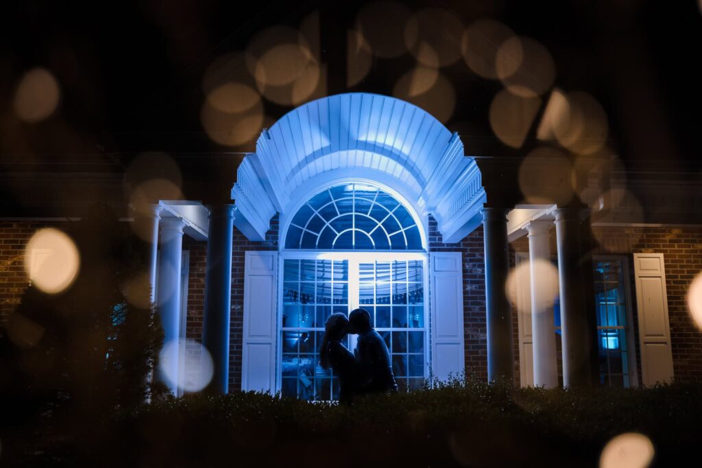 Romantic nighttime portrait of a bride and groom outside the Estate at East Wind, silhouetted beneath the illuminated entrance during an elegant Long Island wedding evening.