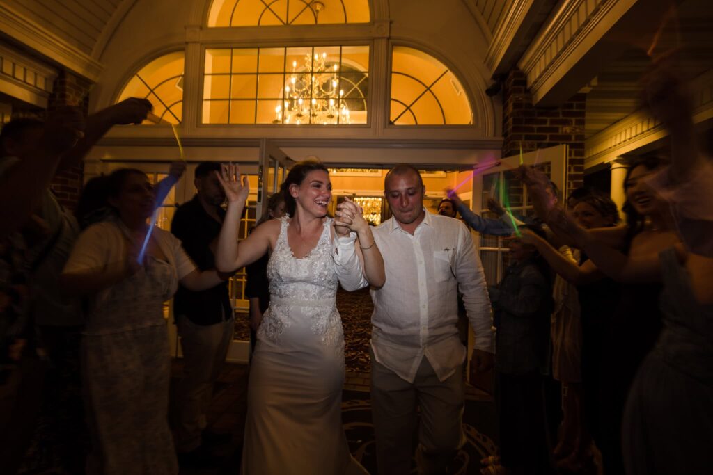 Bride and groom exiting their wedding reception at night, celebrating with guests beneath the glowing entrance of the elegant Long Island estate.