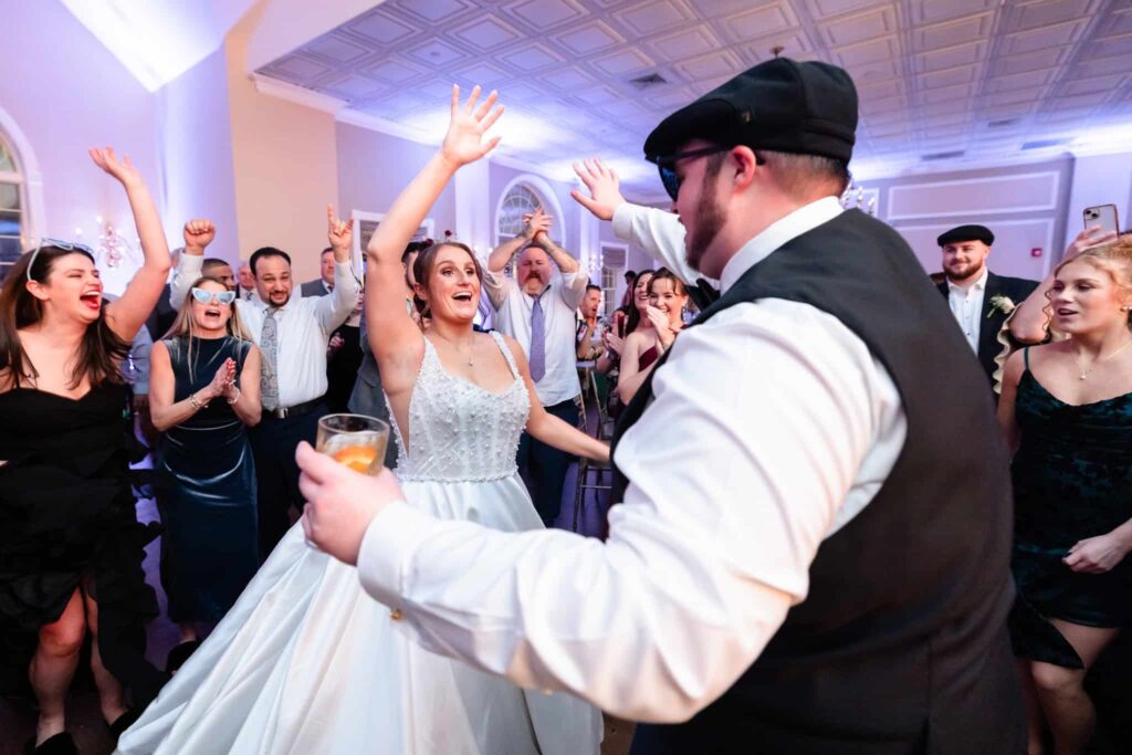 Bride and groom dancing together on a packed dance floor during an Estate at East Wind wedding reception, surrounded by cheering guests inside the elegant Long Island ballroom.