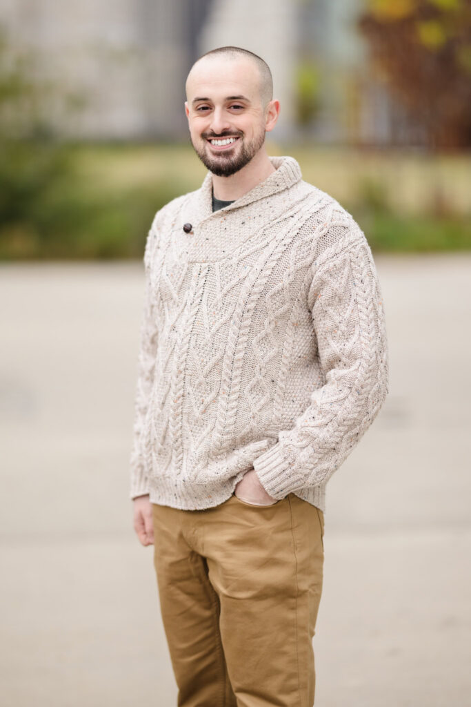 Groom portrait during fall engagement photos in DUMBO, featuring a textured knit sweater and soft November morning light in Brooklyn.