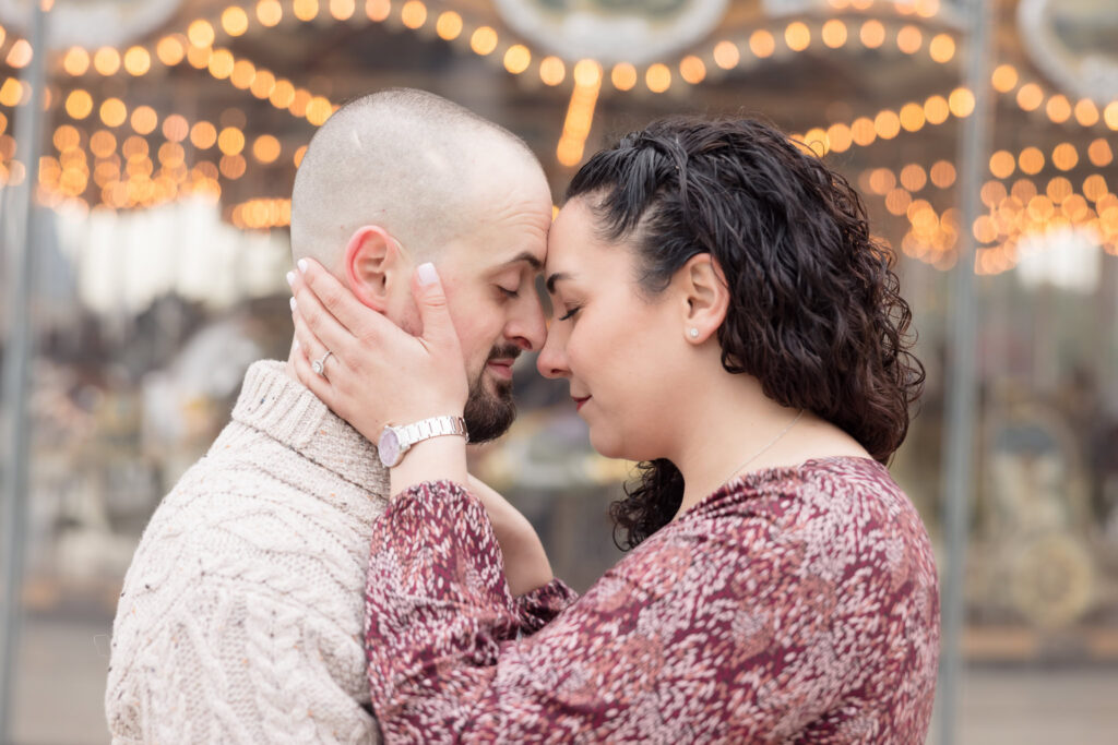 Intimate forehead touch in front of Jane’s Carousel during fall engagement photos in DUMBO, with warm carousel lights glowing behind this November Brooklyn engagement session.