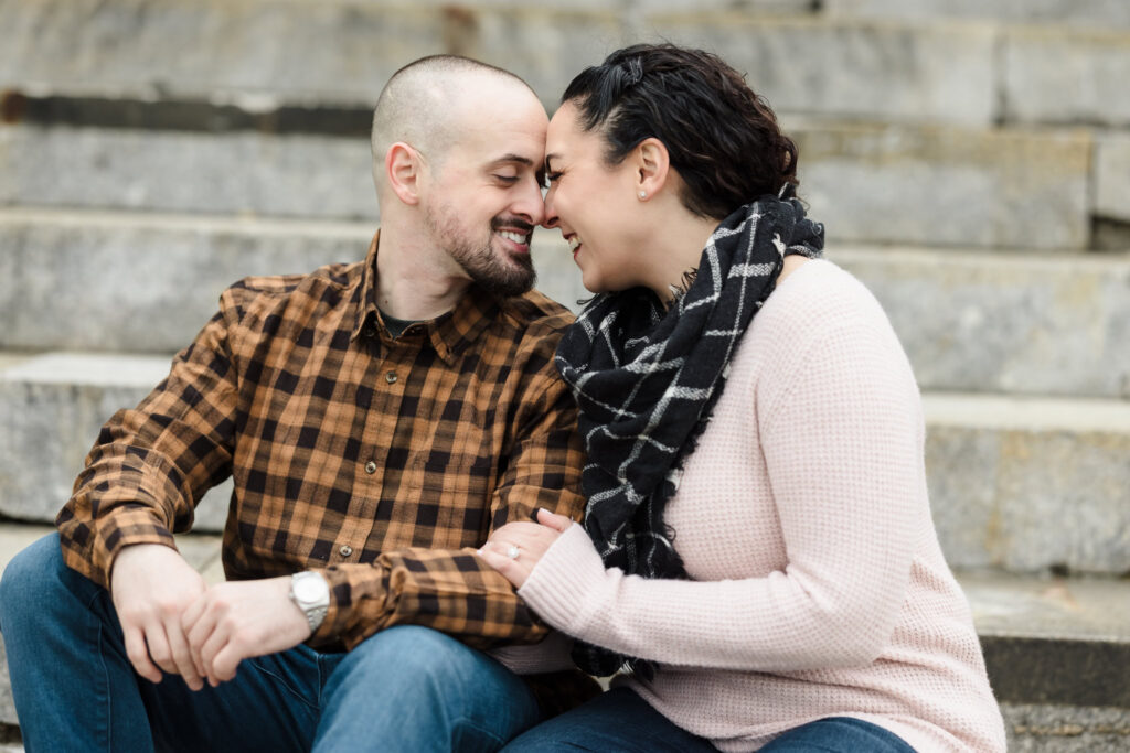 Couple sitting on stone steps during a cozy autumn engagement session in Brooklyn, sharing a quiet smile in soft November light.