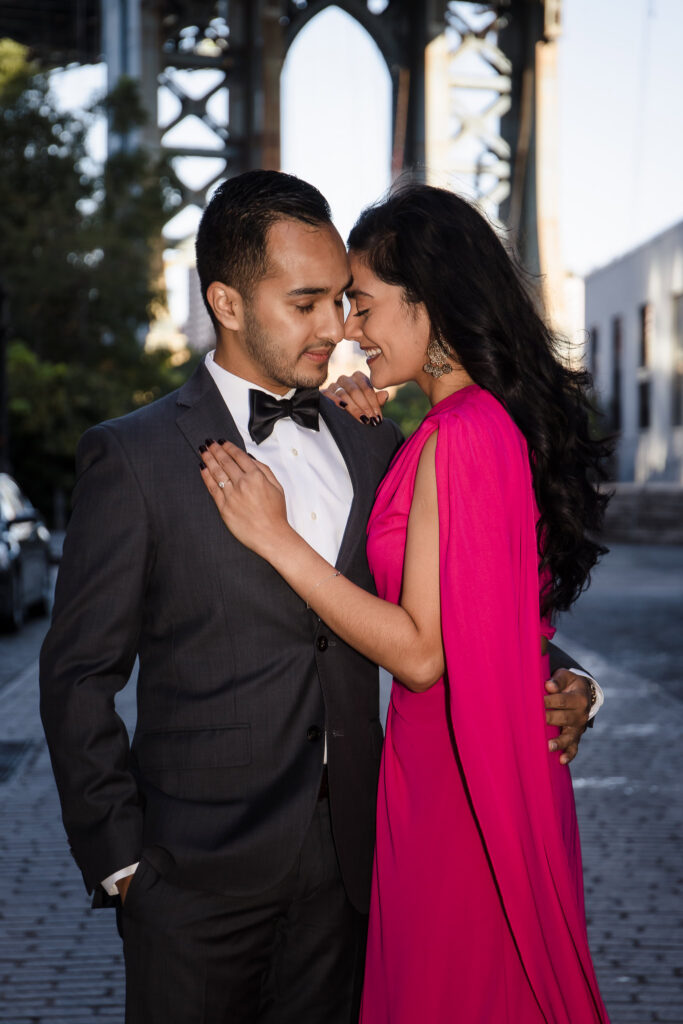 Luxury engagement photos in DUMBO featuring Mahati in a vibrant sari inspired engagement dress and Winston in a tuxedo beneath the Manhattan Bridge on Washington Street during a morning engagement session.