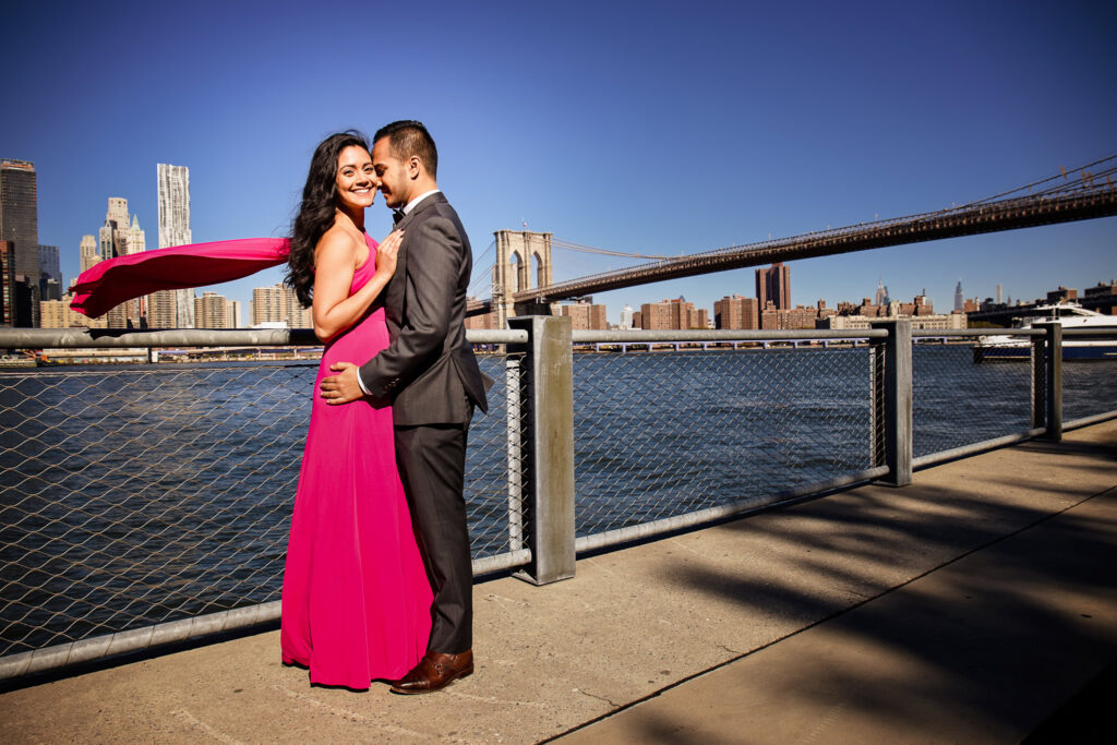 Luxury engagement photos in DUMBO along the Brooklyn waterfront, with Mahati’s flowing sari inspired engagement dress set against the Brooklyn Bridge and Manhattan skyline backdrop.