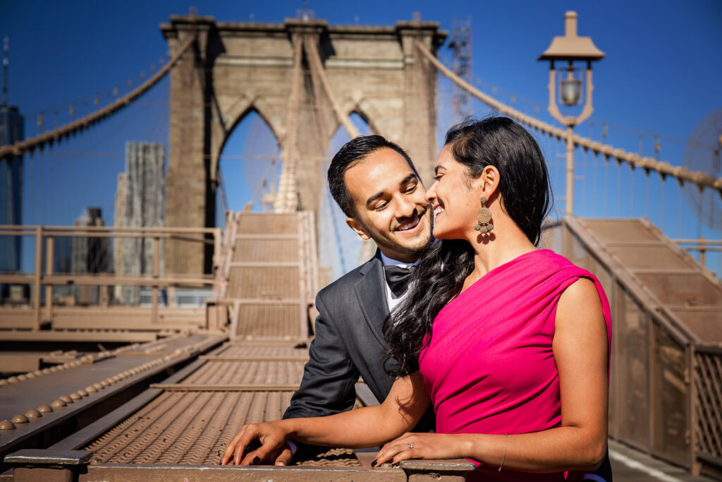 Mahati and Winston sharing a joyful moment on the Brooklyn Bridge, captured during their luxury engagement session in DUMBO with architectural lines and skyline views behind them.