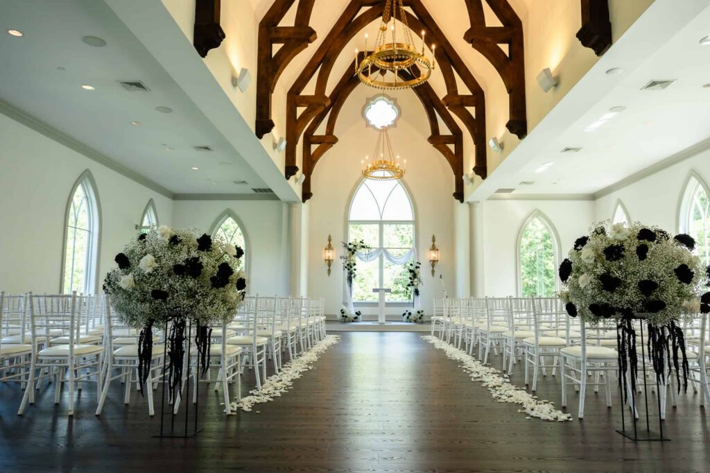 Wide view of the chapel at a Park Chateau wedding in East Brunswick, NJ, with arched windows, exposed beams, and floral-lined aisle at this luxury estate venue.