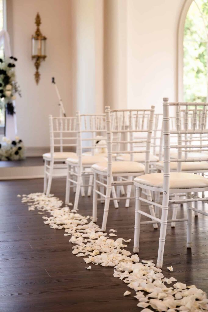 White ceremony chairs lined with rose petals inside the chapel in East Brunswick, NJ, showcasing the refined elegance of this Central New Jersey wedding venue.