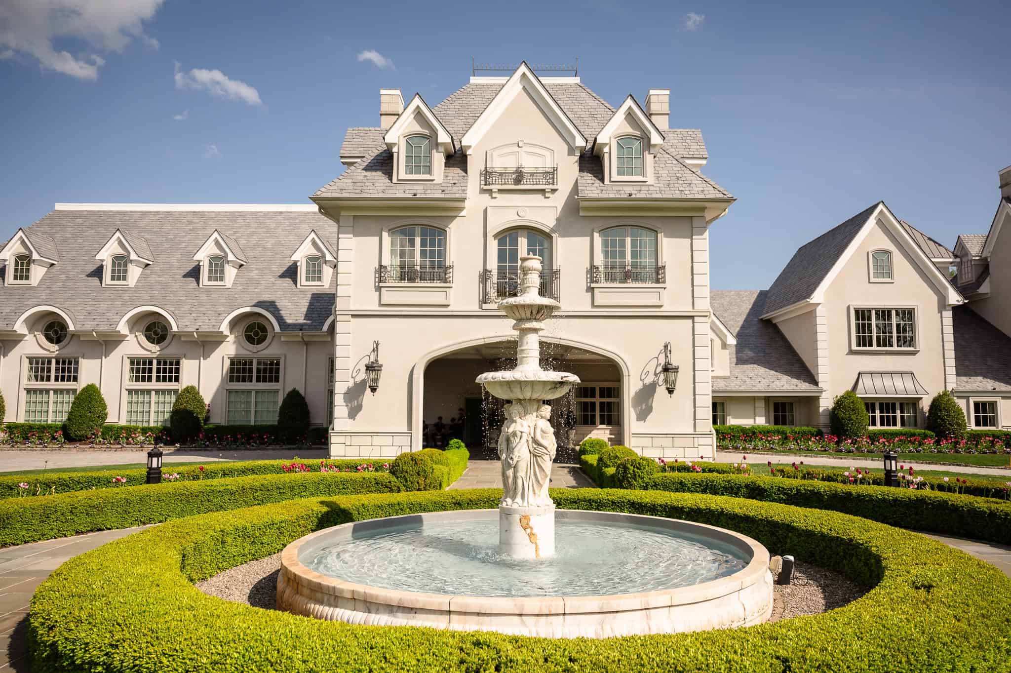Front facade of Park Chateau Estate and Gardens with central fountain and manicured hedges in East Brunswick, NJ, a signature luxury New Jersey wedding venue.