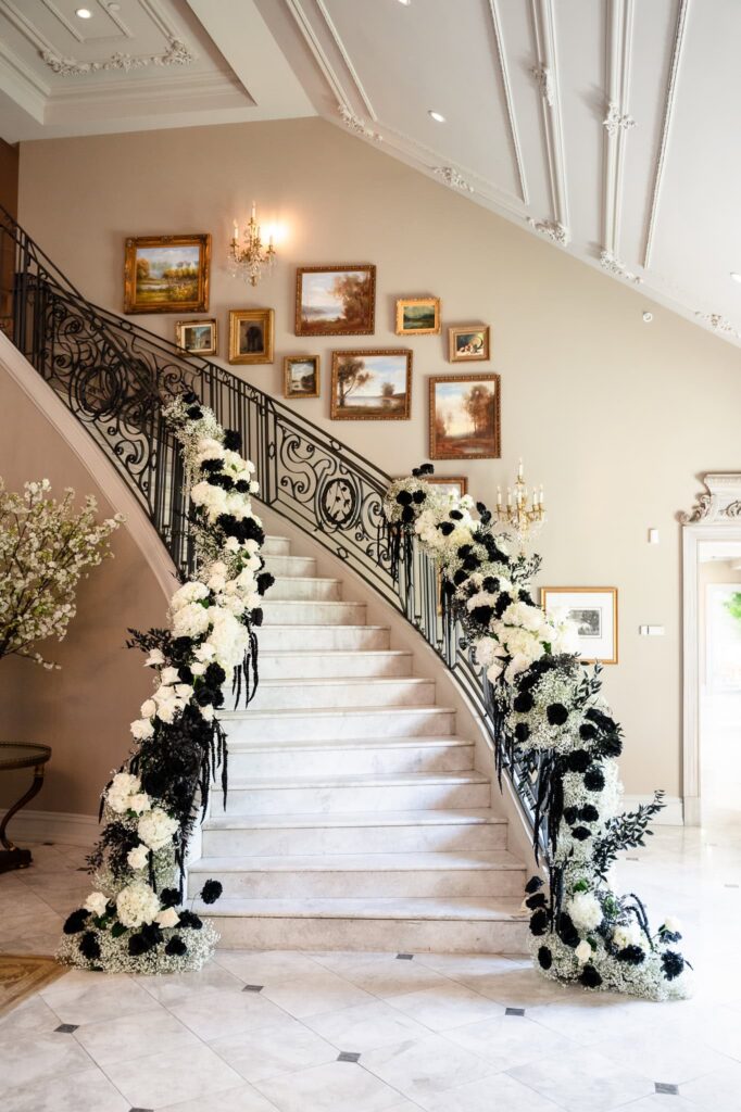 Grand marble staircase with black and white floral installations at Park Chateau Estate and Gardens in East Brunswick, NJ, a dramatic focal point for a luxury estate wedding.