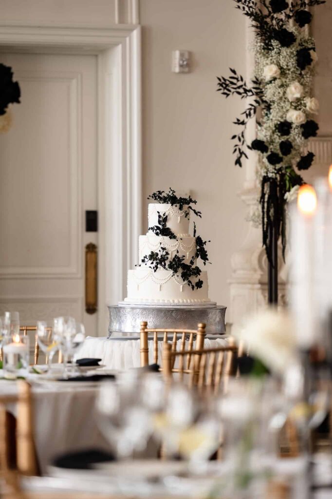 Three-tier white wedding cake with black floral accents displayed in the Park Chateau ballroom, an elegant reception detail at this East Brunswick NJ estate wedding venue.