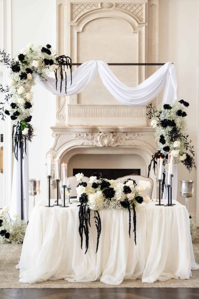 Sweetheart table with black and white florals framed by fireplace and draped backdrop at Park Chateau Estate and Gardens, a luxury New Jersey wedding venue in East Brunswick.